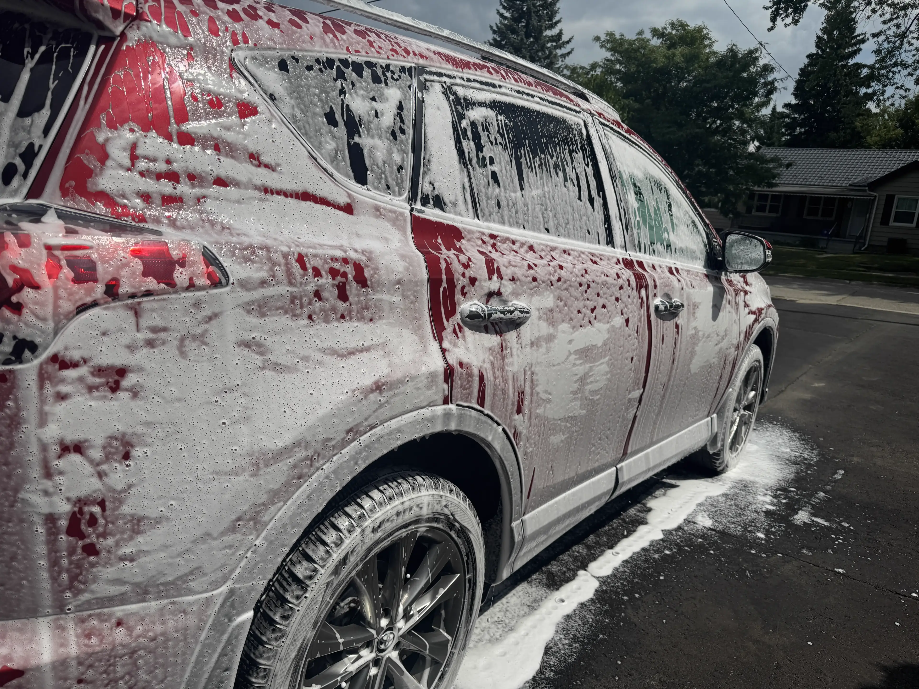 Foam-covered red SUV being detailed in a driveway